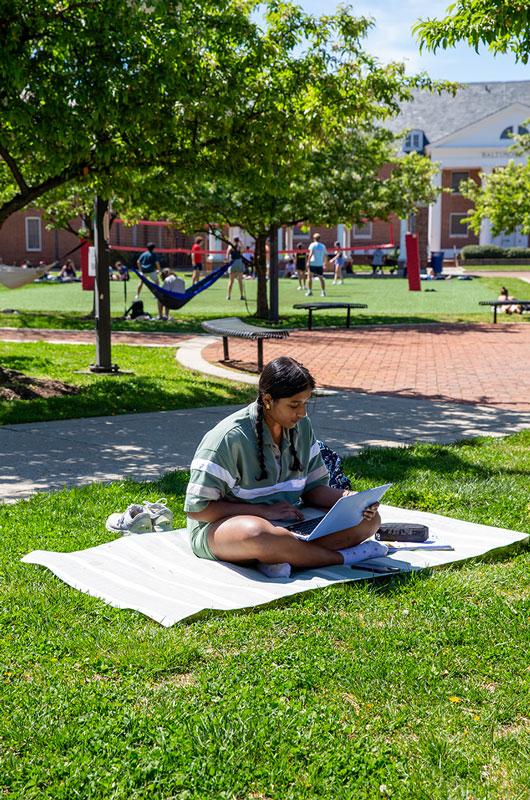 A student sits cross-legged on a blanket in Washington Quad, working on a laptop.