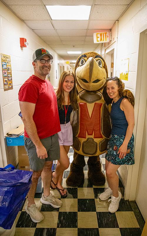 A student and their family posing with the Testudo mascot in a residence hall hallway.