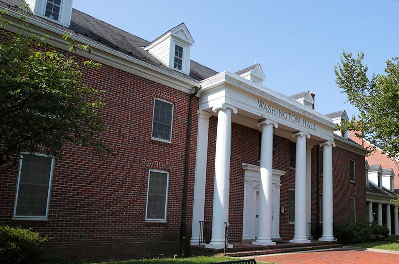 Exterior of Washington Hall, a brick building with four large white pillars and roof dormers.