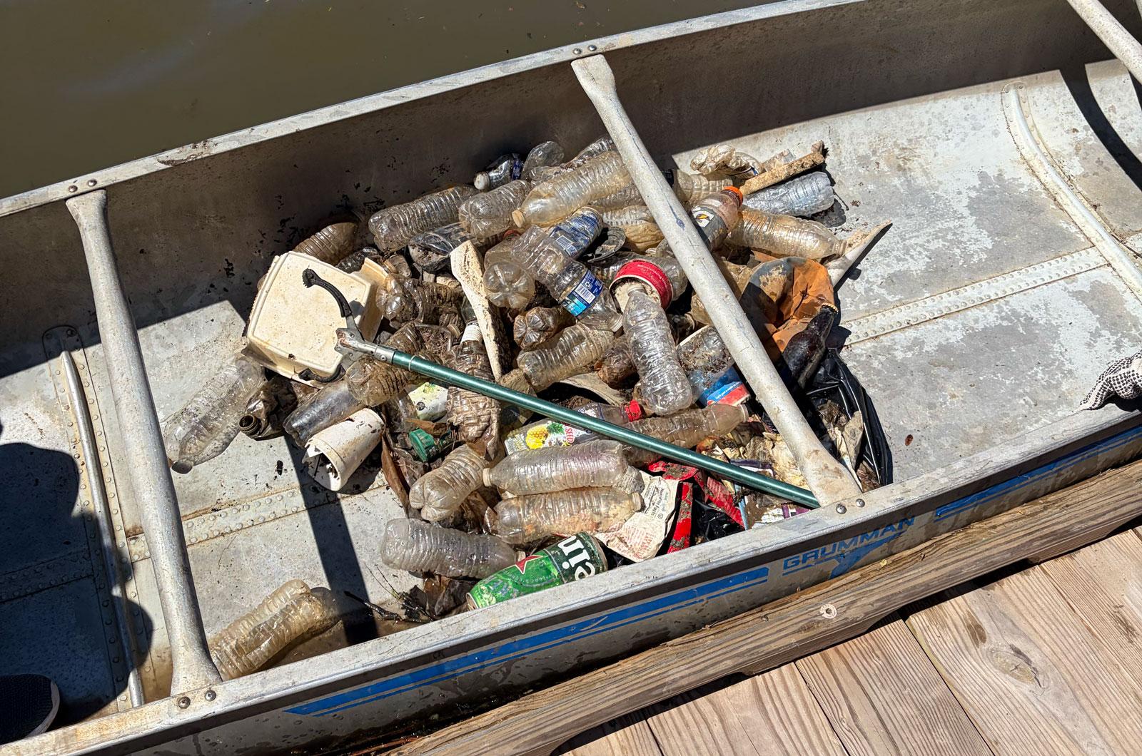 A canoe at a wooden dock is filled with plastic bottles and trash collected from the water.