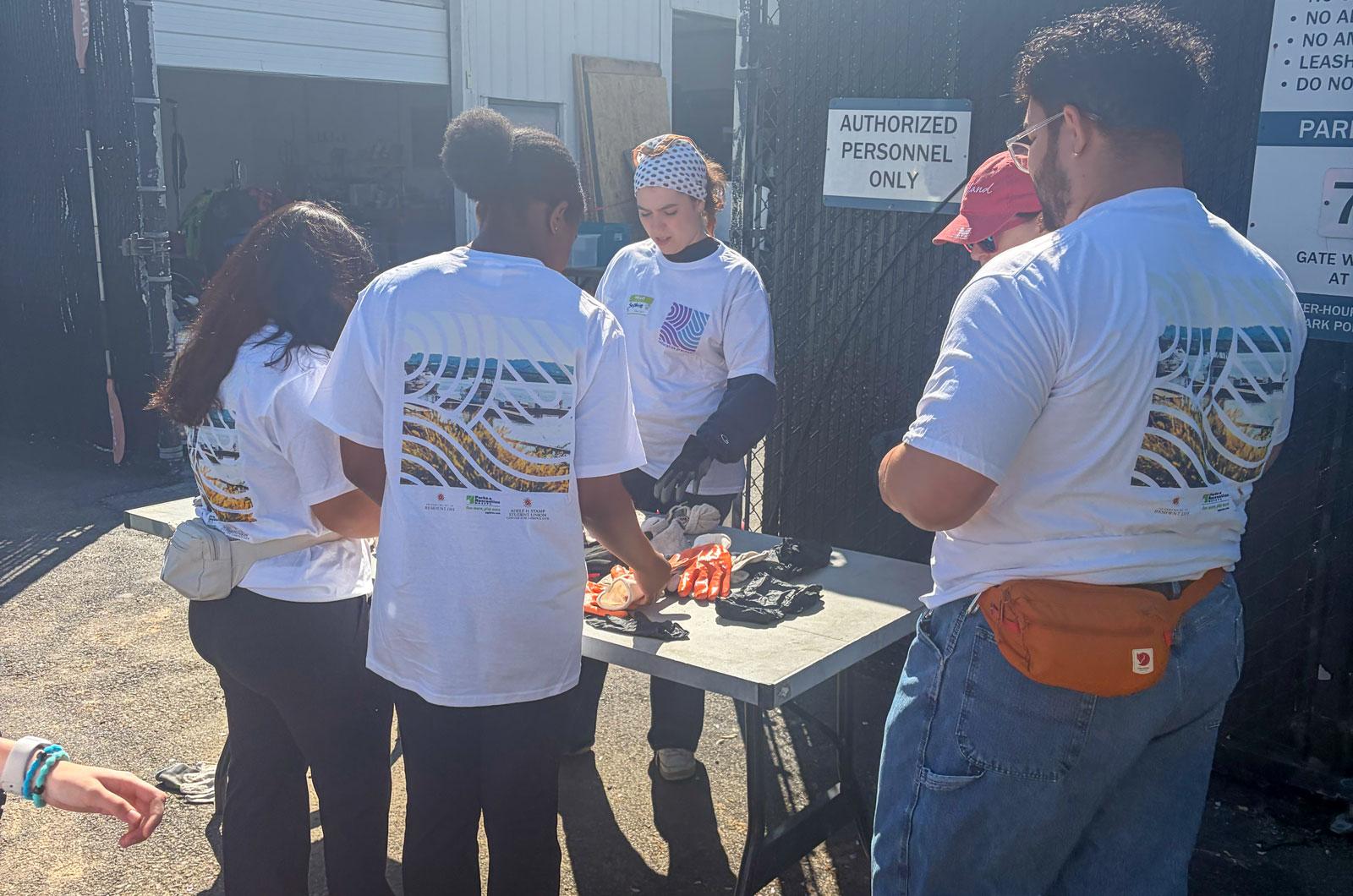 Four volunteers in matching t-shirts gather around a table to pickup work gloves outdoors.