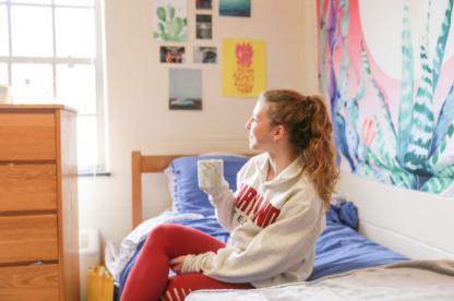 student sitting on their bed with a coffee mug staring our the window