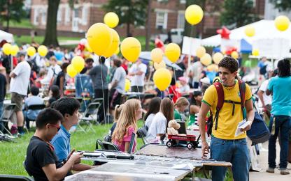 student wearing Brazil national soccer jersey checking out a booth during the first look fair, balloons and tents blurred in the background