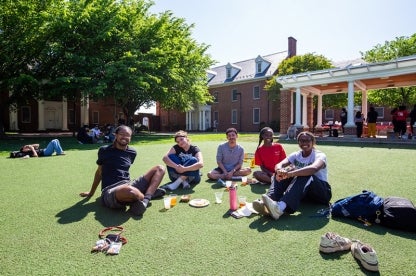 5 students lounge on the grass in a semi-circle outside Howard Hall during the South Campus Block Party.