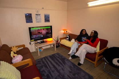 two roommates talk and laugh while siting on a couch in their Leonardtown apartment living room.
